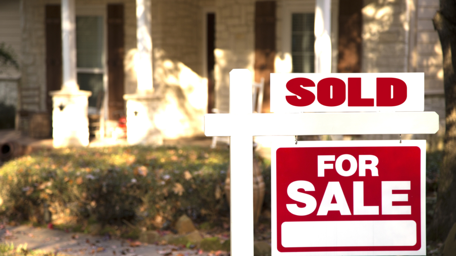 Home for sale with red and white real estate sign during the fall season.  Fall season with leaves on ground.  Front porch and windows in background.  Residential neighborhood.  Moving house, relocation concept.